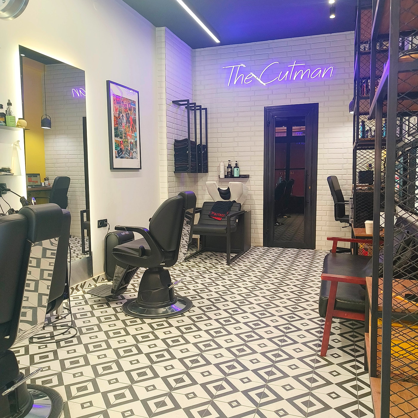 Το εσωτερικό του THE CUTMAN: το neon ταμπελάκι The Cutman, οι μαύρες καρέκλες κουρείου και το ασπρόμαυρο γεωμετρικό δάπεδο