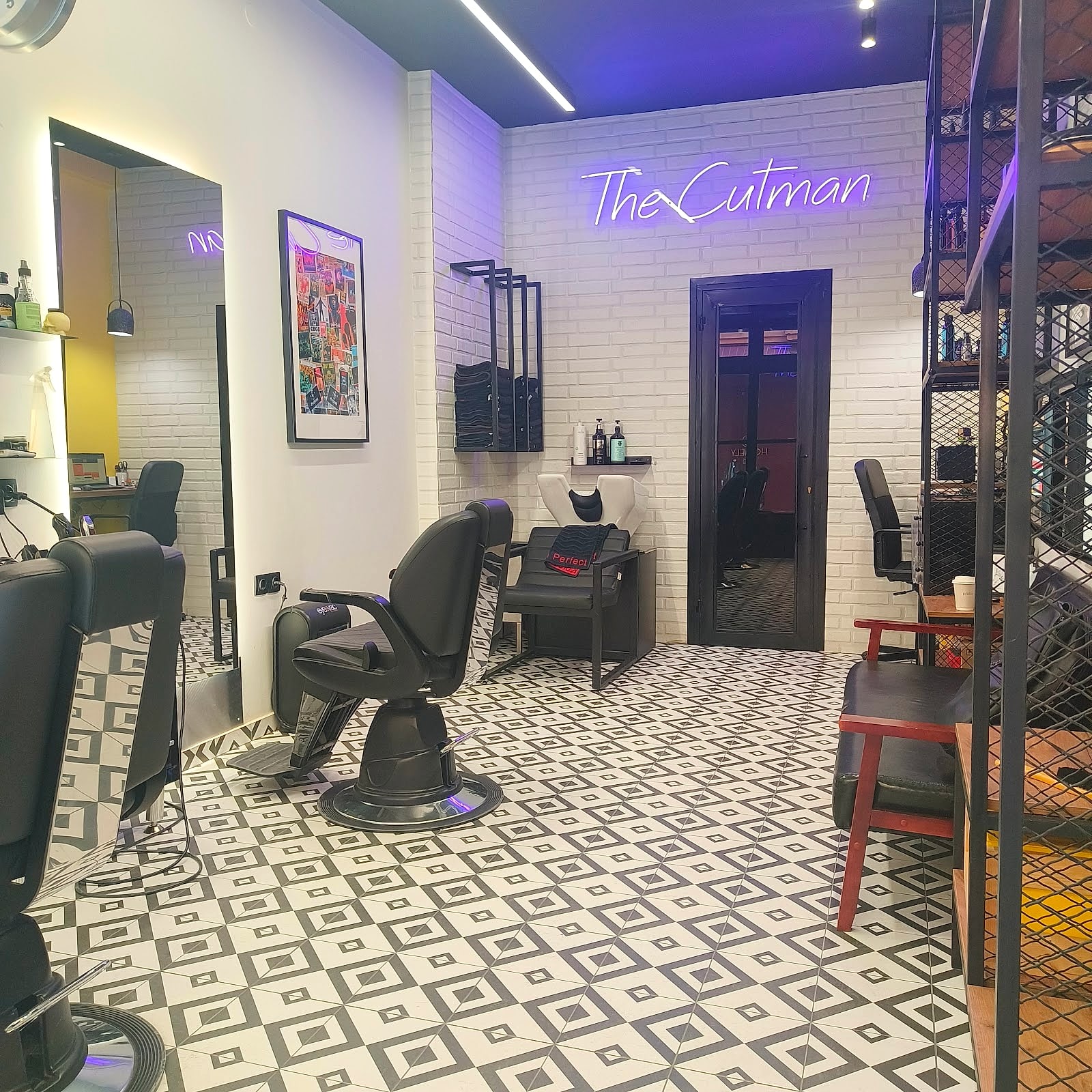 Το εσωτερικό του THE CUTMAN με το neon σήμα, τα ασπρόμαυρα γεωμετρικά πλακάκια και τις καρέκλες barber